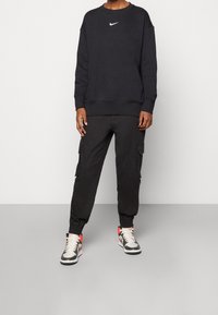 Sudadera negra con el logo blanco de Nike, pantalones cargo negros con bolsillos laterales y zapatillas altas con acentos rojos. Ajuste relajado y casual.