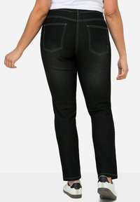 Jeans in denim nero con una vestibilità aderente, caratterizzati da tasche posteriori, cuciture a contrasto e una texture liscia. Abbinati a scarpe da ginnastica bianche.