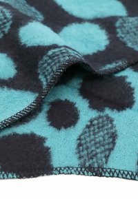 Coperta di lana color teal con grandi pois scuri e un motivo testurizzato. I bordi presentano cuciture visibili, aggiungendo un dettaglio dimensionale.