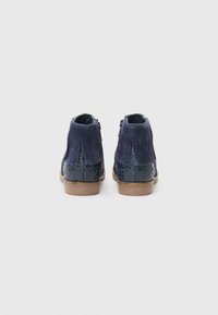 Bottines en suede bleu marine avec des franges à l'arrière, des côtés en imprimé léopard bleu foncé à texture contrastante et une semelle en caoutchouc marron.