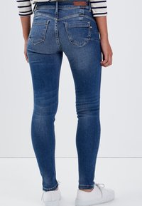 Dunkelblaue Jeans aus Denim mit einer taillierten Passform, fünf Taschen und dezenten Abnutzungen an den Oberschenkeln. Die Nähte stehen im Kontrast zum Stoff.