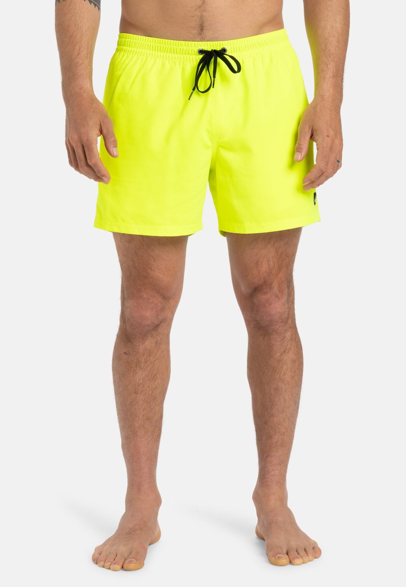Neon sárga fürdőshorts rugalmas derékkal és fekete zsinórral, oldalsó logóval, sima anyagból készült, térd feletti hosszúságú.