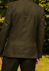 Ciemnozielona marynarka o jodełkowym wzorze, gładkiej fakturze, dopasowanym kroju, zapięciem na jeden guzik oraz subtelnymi zdobieniami na ramionach.
