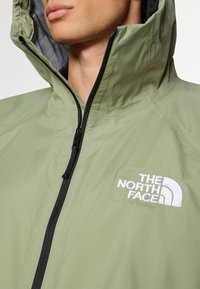 Hellgrüne Jacke mit Reißverschluss, hohem Kragen und Mesh-Futter. Akzentuiert mit einem weißen Logo auf der Brust. Leichtes Material.