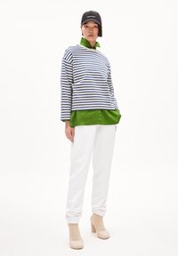 Maglione a righe maniche lunghe in bianco e blu, indossato sopra una camicia colletto verde; abbinato a pantaloni sportivi bianchi e stivali beige con tacco.