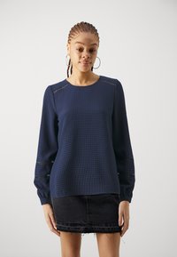 Navy blue long-sleeve top with a textured check pattern, features lace inserts at sleeve cuffs, paired with a black denim skirt.