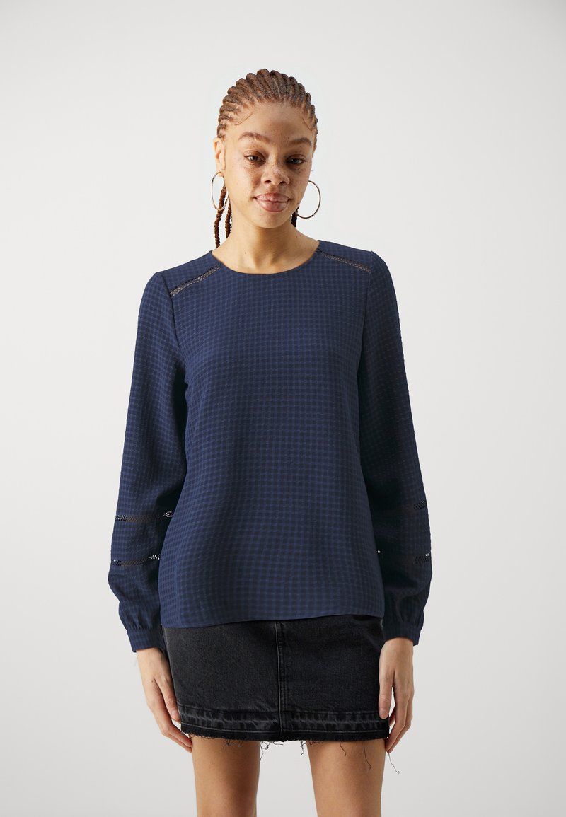 Navy blue long-sleeve top with a textured check pattern, features lace inserts at sleeve cuffs, paired with a black denim skirt.