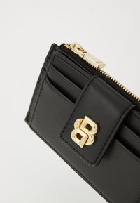 Portafoglio in pelle nera con chiusura a zip, numerosi scomparti per carte e un accento logo in tono oro. Texture liscia con design strutturato.