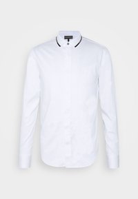 Vit skjorta med knappar tillverkad av mjukt tyg, med en kontrasterande svart kant på kragen och långa ärmar. Slim fit design.