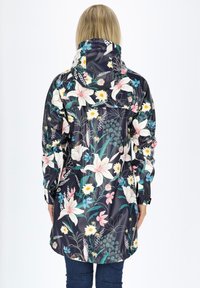 Impermeabile floreale con sfondo blu scuro, caratterizzato da grandi gigli bianchi e fiori multicolori, dotato di cappuccio regolabile e polsini elastici.