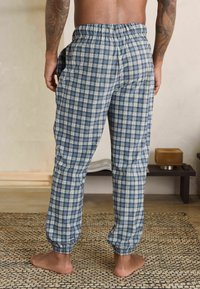 Zilā un baltā kvadrātveida jogger bikses ar elastīgu jostu, sānu kabatām un elastīgiem aproces. Kokvilnas audums ar maigu tekstūru.