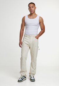 Heledad beežid püksid lõdva lõikega, peente õmblusdetailidega ja küljetaskutega, kombineeritud valge topi ja rohelise aktsendiga tossudega.