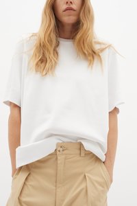 Hvid kortærmet t-shirt med afslappet pasform, der har en rund halsudskæring og glat stof. Kombineret med beige high-waisted bukser.