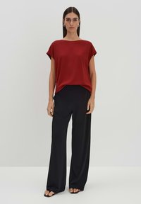 Rotes Kurzarmoberteil kombiniert mit schwarzen, weiten Hosen. Glatter Stoff, lockere Passform und minimalistisches Design. Schwarz offene Sandalen.