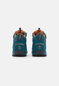 Teal wandelschoenen met oranje accenten, mesh textuur, hoge enkelondersteuning en robuuste zool. Voorzien van logo en reflecterende details aan de zijkanten.