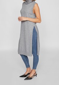 Grå ärmlös polokragnattklänning med sidoklipp, kombinerad med blå skinny jeans och svarta spetsiga klackar. Mjuk stickad textur.