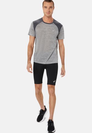Gray striped athletic t-shirt with dark shoulder accents, paired with black compression shorts and black running shoes.