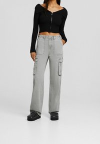 Top corto a maniche lunghe a coste nere con zip, abbinato a pantaloni cargo larghi grigi con grandi tasche e vestibilità rilassata. Scarpe nere.