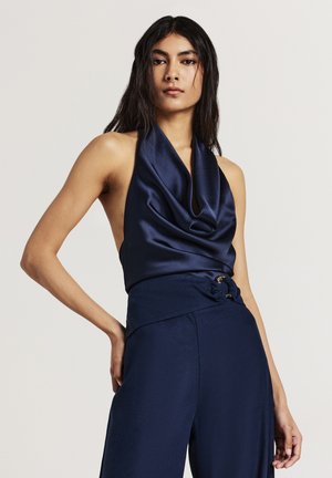 Haut halter en satin marine avec un décolleté drapé, complété par un pantalon marine taille haute avec un détail froncé et une subtile finition métallique.