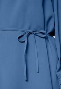 Vestido de tecido azul com um cinto amarrado na cintura, textura suave e um design de corte solto.