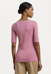 Camisa rosa ajustada com mangas de três quartos e decote arredondado, feita de tecido suave, apresenta detalhes de mangas com punho e um design limpo.