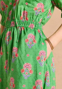 Zielona sukienka w kwiaty wykonana z lekkiego materiału o teksturowanym wykończeniu. Posiada różowe i niebieskie wzory kwiatowe, marszczoną talię oraz kieszenie.