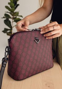 Burgunderfarbene Handtasche mit geometrischem Muster, schwarzem Reißverschluss und Beschlägen, flachem Boden und verstellbarem Schultergurt. Strukturmaterial.