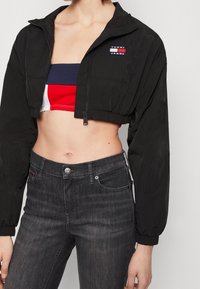 Czarna krótka kurtka z zamkiem z przodu, elastycznymi mankietami i logo "TOMMY JEANS". Nosi się ją na wielokolorowym topie z krótkim rękawem w czerwono-biało-niebieskie paski.