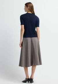 Haut en tricot à manches courtes bleu marine associé à une jupe midi à carreaux gris. La tenue présente une silhouette ajustée et un tissu texturé. Des chaussures noires sont incluses.