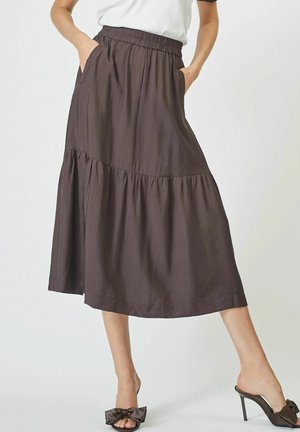 Brown, textured maxi skirt with an elastic waistband, tiered design, side pockets, and a flowy silhouette, paired with brown slide sandals.