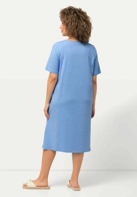 Niebieska bawełniana sukienka t-shirtowa z krótkimi rękawami, luźny krój, sięgająca poniżej kolan, z okrągłym dekoltem. Noszona z jasnymi sandałami.