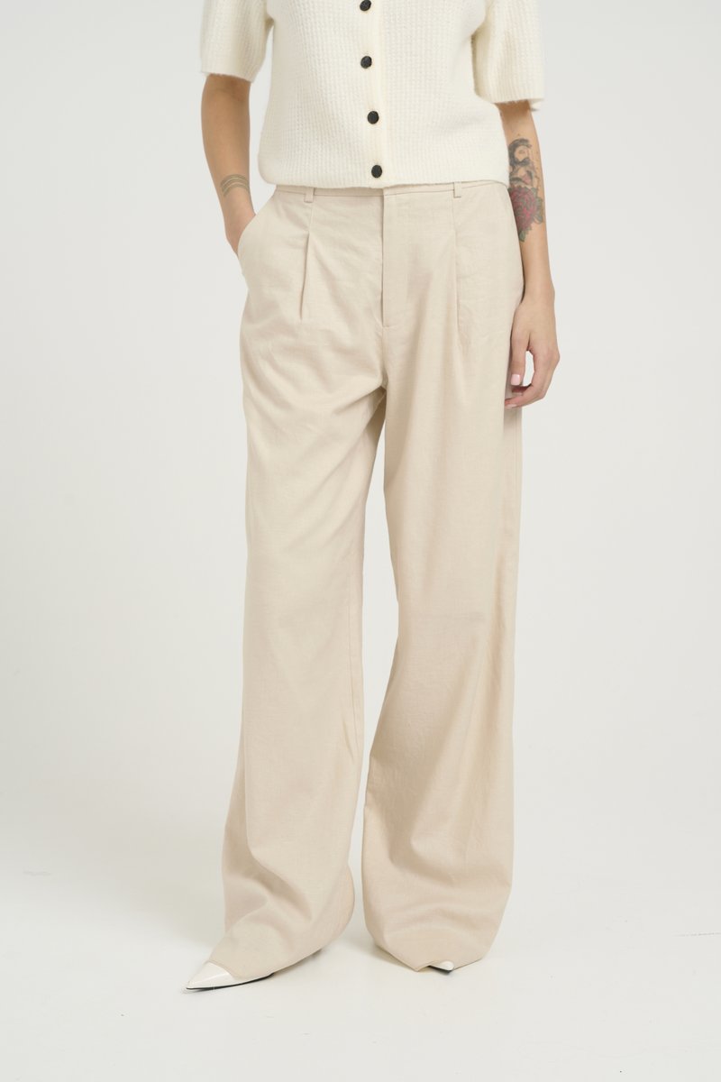 Beige vida byxor med en avslappnad passform, veck framtill och jämn textur. Stylad med en ljus färgad stickad topp och spetsiga klackar.