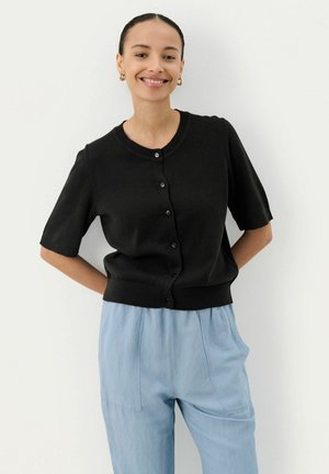 Black knitted short-sleeve cardigan with a round neckline, button closure, and ribbed hem, paired with light blue loose trousers.