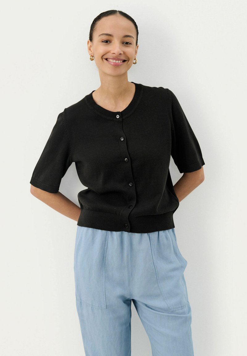 Schwarze gestrickte Kurzarm-Cardigan mit rundem Ausschnitt, Knopfverschluss und geripptem Saum, kombiniert mit hellblauen lockeren Hosen.