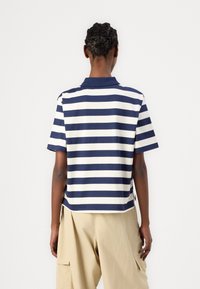 Polo a righe blu navy e bianche con colletto corto, in cotone, orlo dritto, abbinato a pantaloni cargo beige.