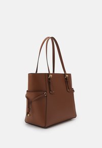 Ruskea nahkainen kantokassi, jossa on kaksi yläkahvaa, sivutasku ja kultausvärejä oleva metallivarustus. Ominaisuuksiin kuuluu jämäkkä muotoilu ja sileä pinta.