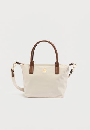 Beige draagtas met bruine leren handvatten en accenten, goudkleurig logo aan de voorkant, afneembare riem en een getextureerd oppervlak.