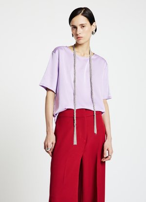 Top lilla a maniche corte con una texture liscia e una scollatura tondeggiante, abbinato a pantaloni rossi a vita alta e gamba larga con un dettaglio lungo in argento.