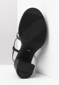 Sandal nero con tacco, dotata di una suola testurizzata, con doppie cinghie e una finitura liscia, su uno sfondo chiaro. Marchio italiano visibile.