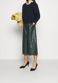 Granatowy sweter, zielone skórzane kuloty, czarne szpiczaste szpilki i żółta torebka w wzory. Sweter ma okrągły dekolt; kuloty wyposażone są w boczne kieszenie.