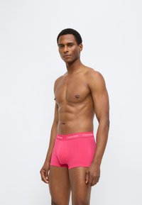 Κόκκινο ελαστικό βαμβακερό εσώρουχο τύπου μπαντόν με μαλακή ζώνη μέσης με την ετικέτα "Calvin Klein." Ο σχεδιασμός έχει εφαρμοστή γραμμή και απαλή υφή.