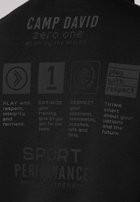 Zwart T-shirt met geprinte graphics op de achterkant, met gemarmerde tekst over sportiviteit en principes van teamwerk. De materialen lijken zacht te zijn.