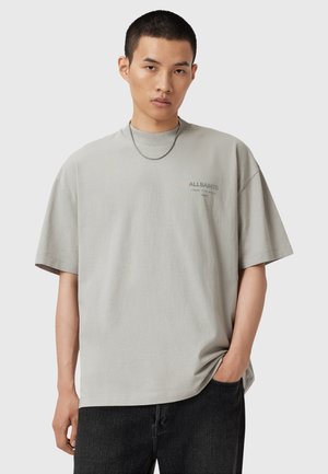 Grå oversized t-shirt med rund halsudskæring, korte ærmer og et lille mærke-logo på brystet. Sammen med mørke denim jeans.