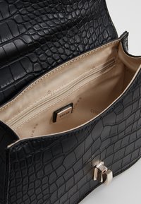 Czarna torba z faux skóry krokodyla z złotymi akcentami i wyraźnym kształtem. Wyłożone wnętrze posiada kieszeń na zamek i markowe detale.