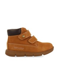 Bottines en daim tan avec un col rembourré marron, deux bandes Velcro et une semelle en caoutchouc. Présente des coutures blanches et un texte en relief sur le côté.