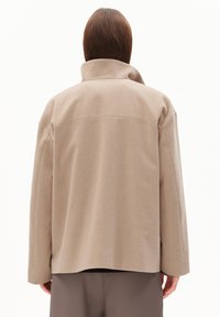 Beige wool blend jacket with a high collar, dropped shoulders, and a relaxed fit. Back view shows minimal seams and a smooth texture.