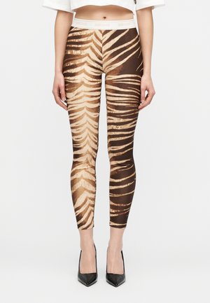 Κολάν στενής εφαρμογής με καφέ και μπεζ ρίγες τίγρης, φορεμένα με ένα crop top σε λευκό χρώμα και μαύρες μυτερές γόβες.