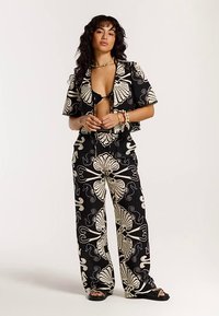 Crni i kremasti usklađeni set koji uključuje kratku majicu s kratkim rukavima i široke hlače s cvjetnim uzorkom. Materijal je lagan i teksturiran.