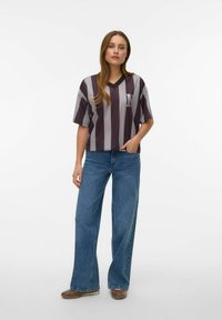 Lühikeste varrukatega V-kaelusega särk, millel on laiad vertikaalsed triibud tumelillas ja helehallis ning "N" logo. Üheskoos kõrge vöökohaga, laiutavate siniste teksadega.