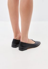 Bottines en cuir noir avec un petit talon, un bout en amande et une finition lisse, arborant un design découpé le long du bord supérieur pour un détail supplémentaire.
